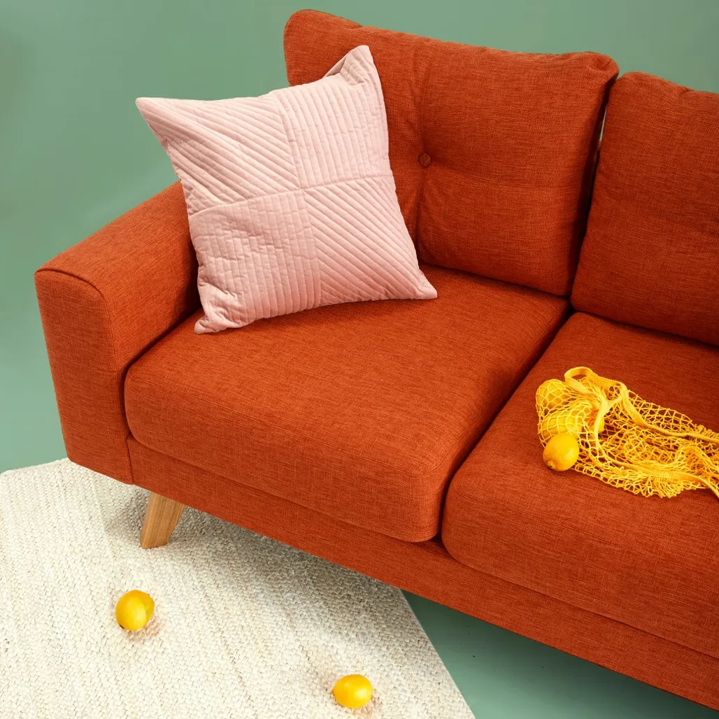 Rust-orange fabric sofa with a quilted pink pillow against a mint-green wall, woven rug with lemons on the floor