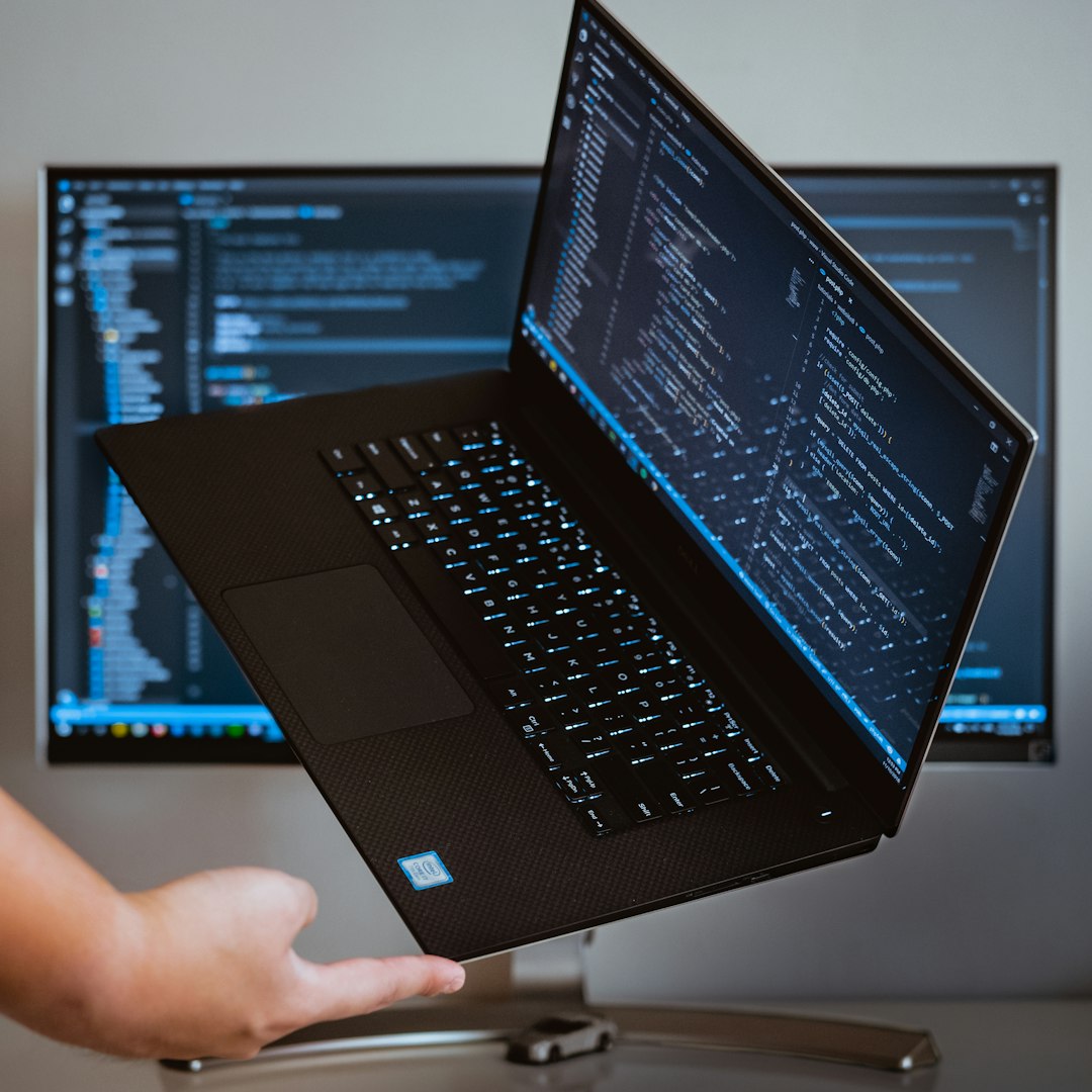 Laptop showing lines of code, held up in front of a second screen